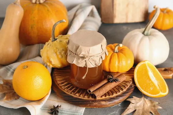 Jar of sweet pumpkin jam with orange and different spices on grey table
