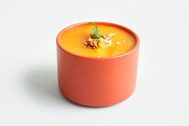 Beyaz arka planda maydanozlu ve cevizli balkabağı kremalı çorba.