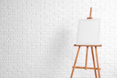 Beyaz tuğla duvarın yanında boş tuval olan ahşap sehpa