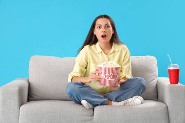 Genç bir kadın patlamış mısırla koltukta mavi arka planda film izlerken şok oldu.