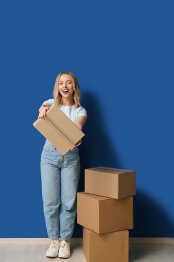 Mavi arka planda karton kutuları olan mutlu genç bir kadın.