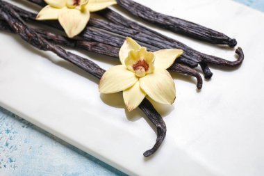 Mavi arka planda aromatik vanilya çubukları ve çiçekleri olan tahta