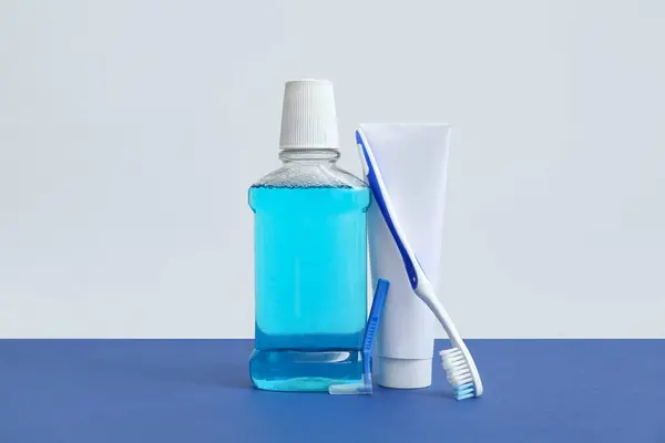 Mouth rinse with toothbrush and toothpaste on color background.