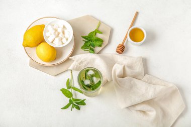 Beyaz zemin üzerinde limon, bal ve şeker küpleriyle bir bardak taze buzlu nane çayı.