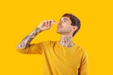 Alerjik genç adam sarı arka planda burun damlası kullanıyor.