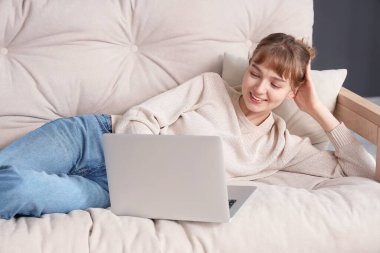 Evde kanepede dizüstü bilgisayar kullanan genç kadın