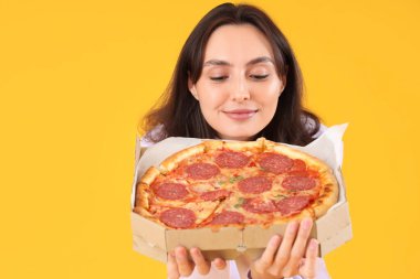 Sarı arka planda lezzetli pepperonili pizzalı genç bayan, yakın plan.