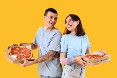 Sarı arka planda lezzetli biberli pizzalı genç çift.