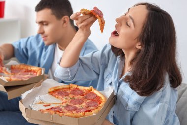 Evde lezzetli biberli pizza yiyen genç çift, yakın plan.