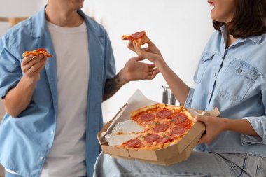 Mutfakta lezzetli biberli pizza yiyen genç çift, yakın plan.