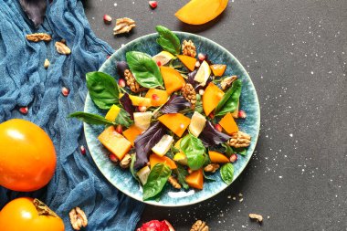 Bir tabak lezzetli salata, hurma, nar tohumu ve siyah arka planda ceviz.