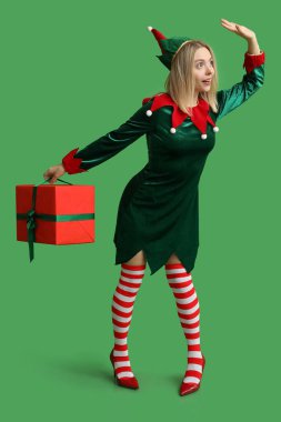 Yeşil arka planda Noel hediyesi kutusu olan elf kostümlü genç bir kadın.