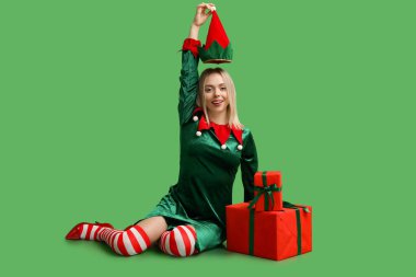 Yeşil arka planda Noel hediyesi kutuları olan elf kostümlü güzel bir genç kadın.