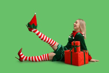 Yeşil arka planda Noel hediyesi kutuları olan elf kostümlü genç bir kadın.