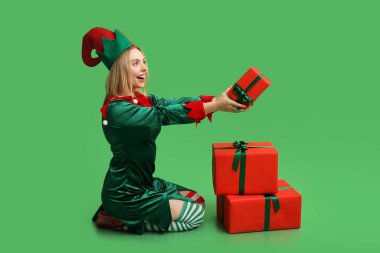 Yeşil arka planda Noel hediyesi kutuları olan elf kostümlü güzel bir genç kadın.