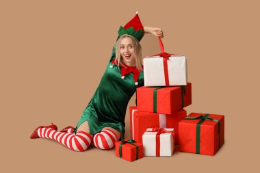 Kahverengi arka planda Noel hediyesi kutuları olan elf kostümlü mutlu genç bir kadın.