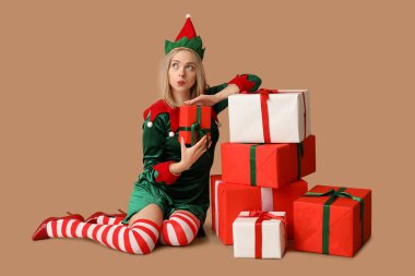 Kahverengi arka planda Noel hediyesi kutuları olan elf kostümlü güzel bir kadın.
