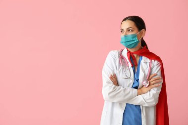 Süper kahraman kostümlü güzel bayan doktor ve pembe arka planda tıbbi maske.