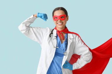 Süper kahraman kostümlü güzel bayan doktor mavi arka planda kaslarını gösteriyor.
