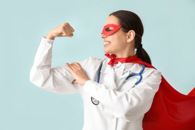 Süper kahraman kostümlü güzel bayan doktor mavi arka planda kaslarını gösteriyor.