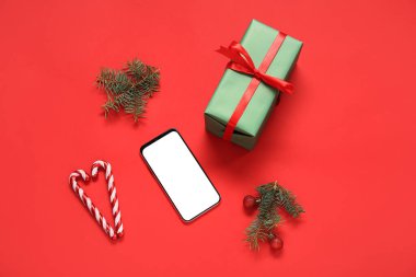 Cep telefonlu Noel hediyesi kutusu, köknar dalları ve kırmızı arka planda şeker kamışı.