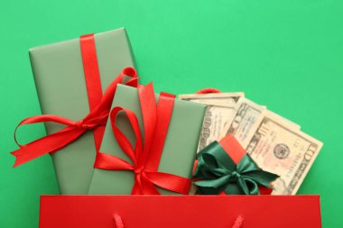 İçinde Noel hediyesi kutuları ve yeşil arka planda para olan alışveriş çantası.