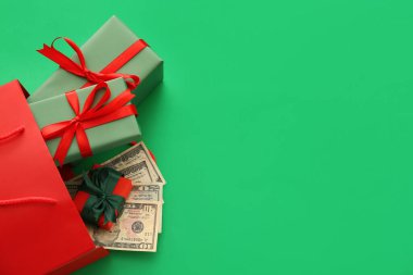 İçinde Noel hediyesi kutuları ve yeşil arka planda para olan alışveriş çantası.
