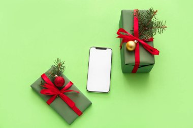 Yeşil arka planda Noel hediyesi kutuları olan cep telefonu.