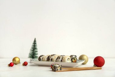 Lezzetli suşi ruloları ve beyaz arka planda Noel topları olan tabaklar.