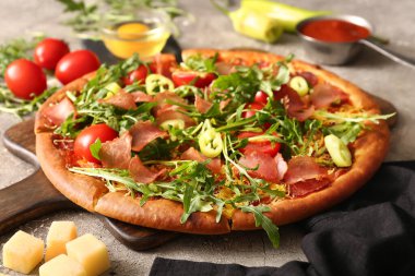 Tahta tahtada domatesli lezzetli pizza ve gri arka planda roka.