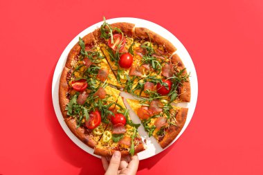 Kadın kırmızı arka planda domatesli ve roka aromalı lezzetli bir pizza yiyor.