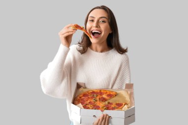 Lezzetli pizza yiyen ve beyaz arka planda karton kutu tutan genç bir kadın.