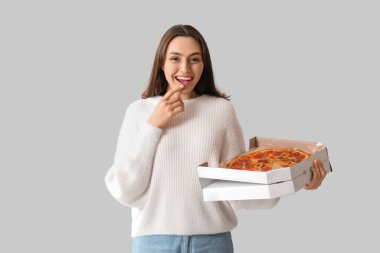 Genç bir kadın beyaz arka planda lezzetli pizzayla dolu karton bir kutu tutuyor.