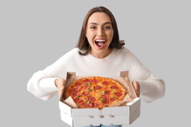 Genç bir kadın beyaz arka planda lezzetli pizzayla dolu karton bir kutu tutuyor.