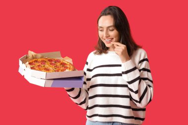 Elinde kırmızı arka planda lezzetli pizzalar olan karton kutu tutan genç bir kadın.