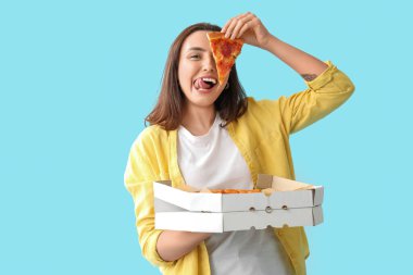 Elinde mavi arka planda lezzetli pizzayla karton kutu tutan genç bir kadın.