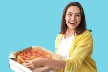Elinde mavi arka planda lezzetli pizzayla karton kutu tutan genç bir kadın.