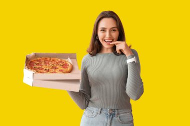 Sarı arka planda lezzetli pizzalı mukavva kutu tutan mutlu genç kadın.