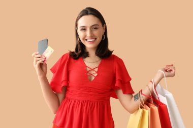 Kredi kartı, cep telefonu ve bej arka planda alışveriş torbaları olan genç bir kadın.