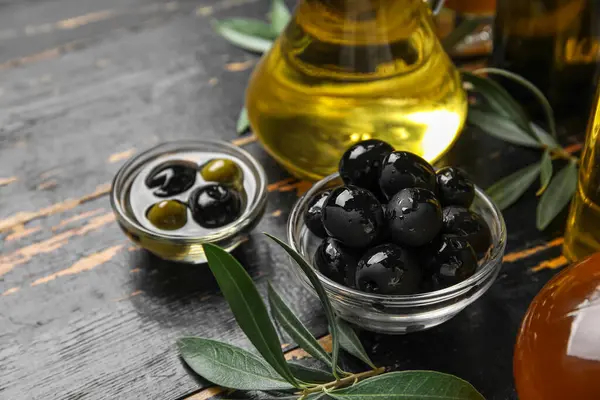Bowls with fresh olives and oil on black wooden background