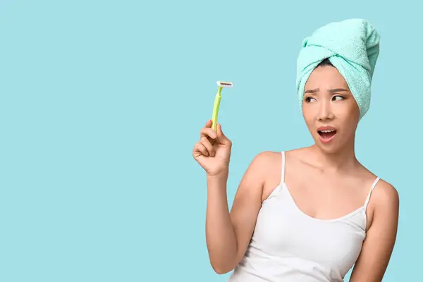 Shocked young Asian woman with razor on blue background