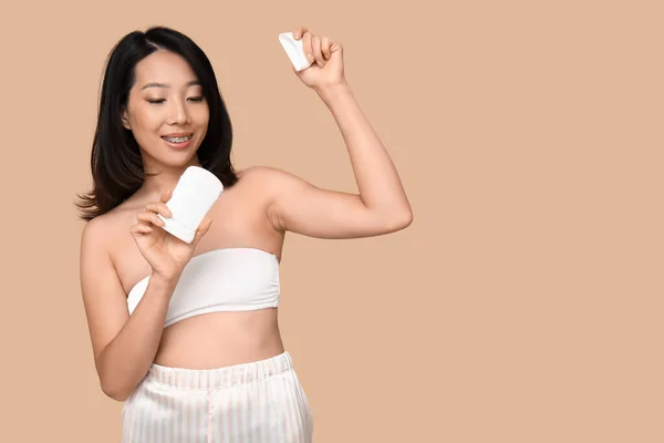 Young Asian woman with deodorant on brown background