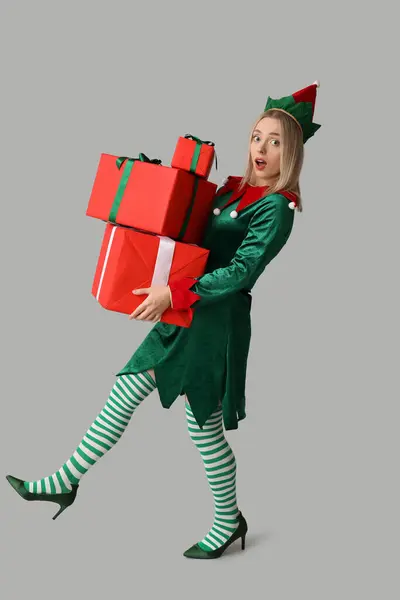 Emotional young woman in elf costume with Christmas gift boxes on white background