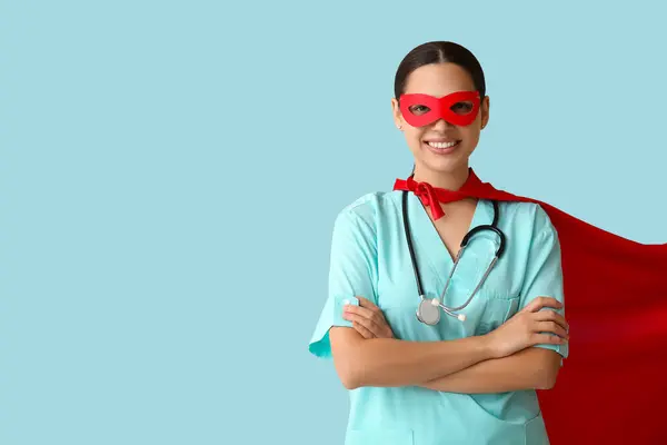 Young female doctor in superhero costume on blue background