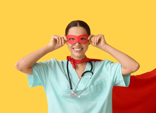 Young female doctor in superhero costume on yellow background