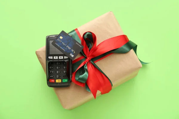 Payment terminal with credit card and Christmas gift box on green background