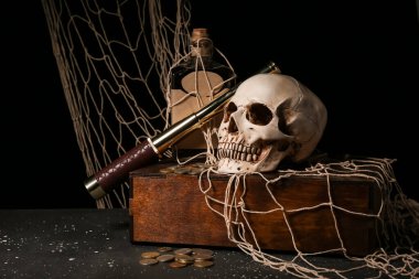 Casus gözlüklü korsan sandığı, insan kafatası, siyah arka planda bir şişe rom ve bozuk para.