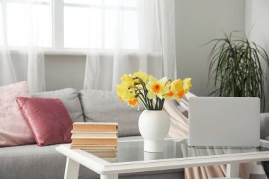 Modern laptop, narsis çiçekli vazo ve oturma odasındaki cam sehpanın üzerinde kitaplar.
