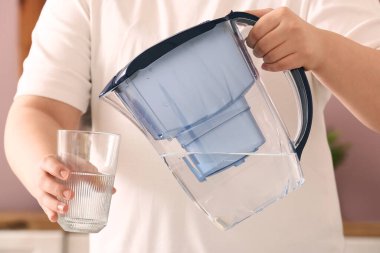 Woman pouring pure water from filter jug into glass clipart