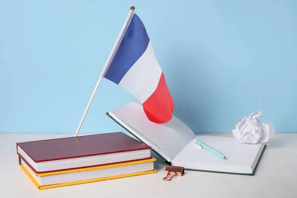 Flag of France with books and crumpled paper on table near blue wall